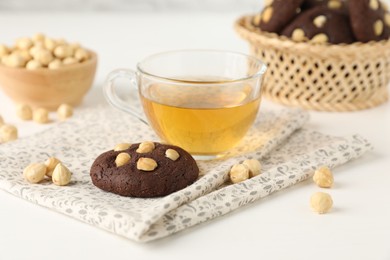 Photo of Tasty chocolate cookies with hazelnuts and tea on white table, closeup