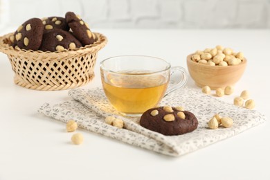 Photo of Tasty chocolate cookies with hazelnuts and tea on white table, closeup