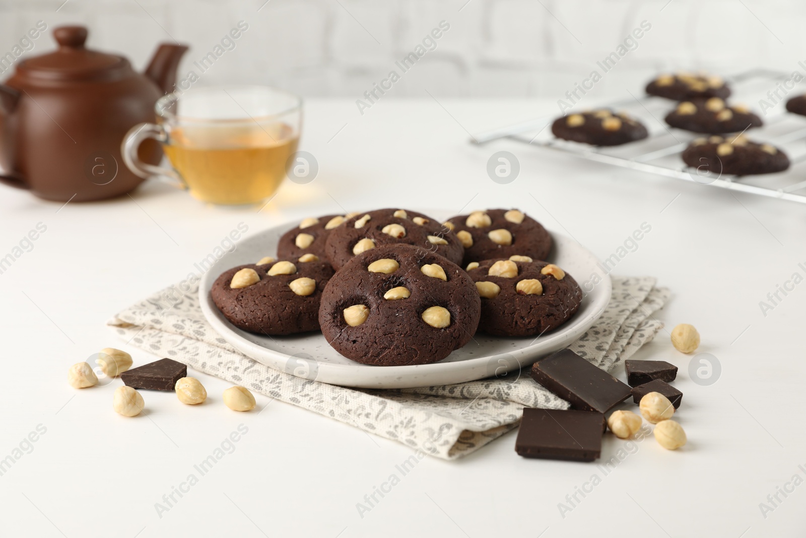 Photo of Tasty chocolate cookies with hazelnuts and tea on white table, closeup