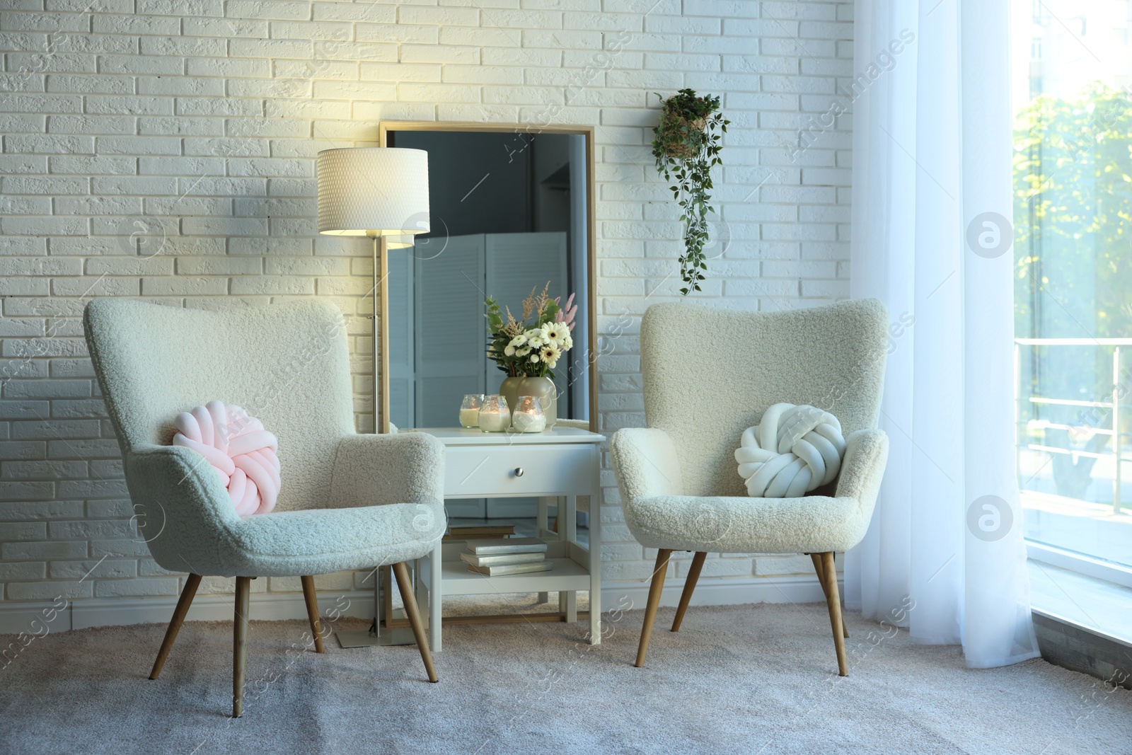 Photo of Soft armchairs, side table, mirror and floral decor in room