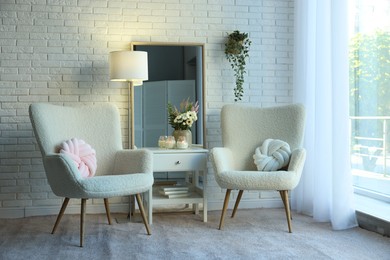 Photo of Soft armchairs, side table, mirror and floral decor in room