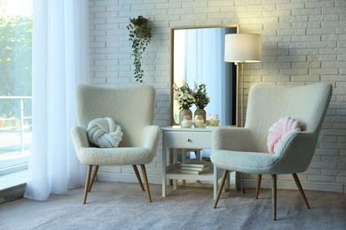 Photo of Soft armchairs, side table, mirror and floral decor in room