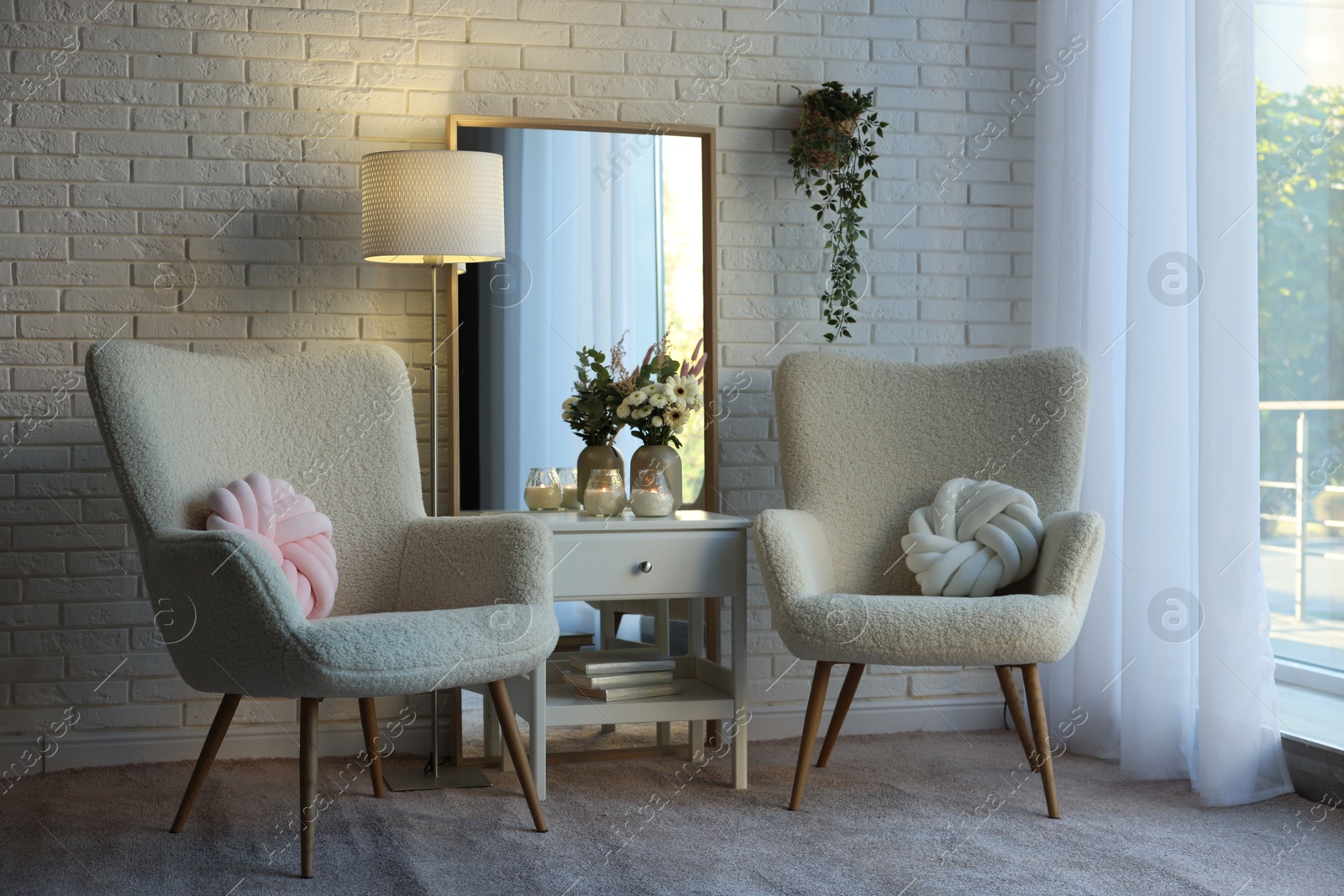 Photo of Soft armchairs, side table, mirror and floral decor in room