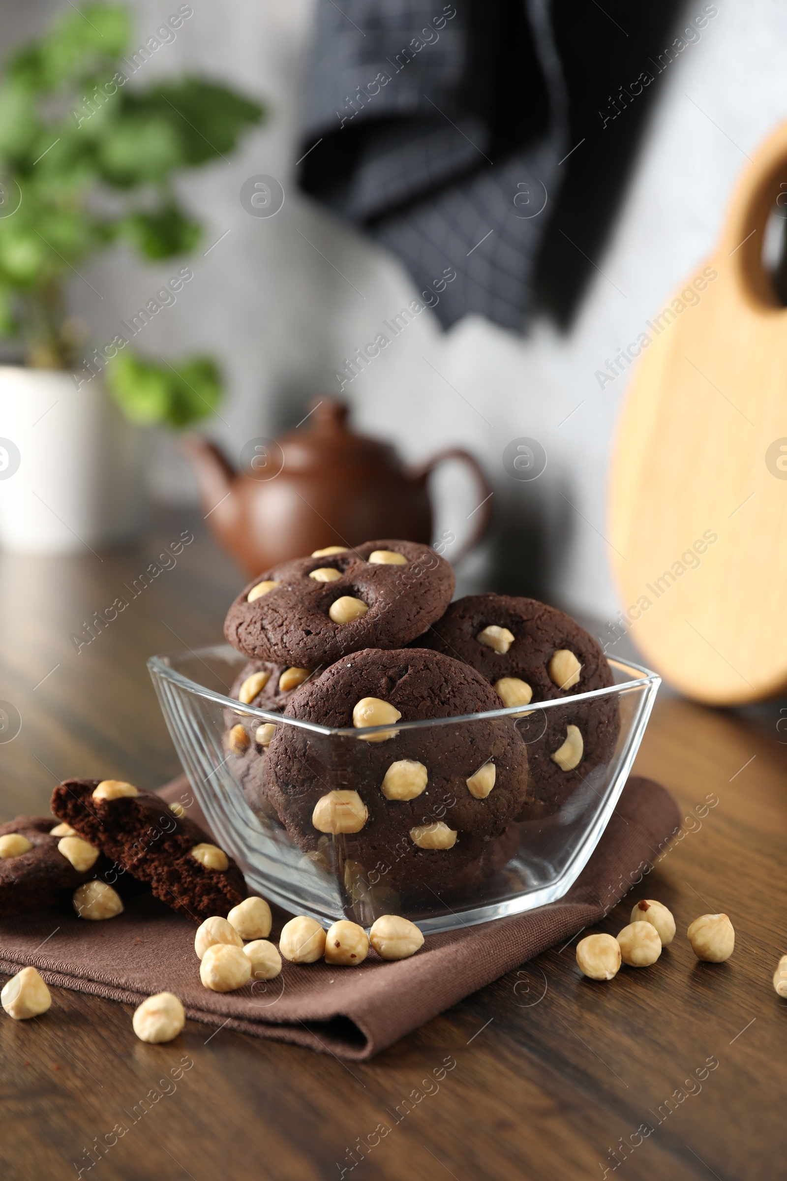 Photo of Tasty chocolate cookies with hazelnuts in bowl on wooden table