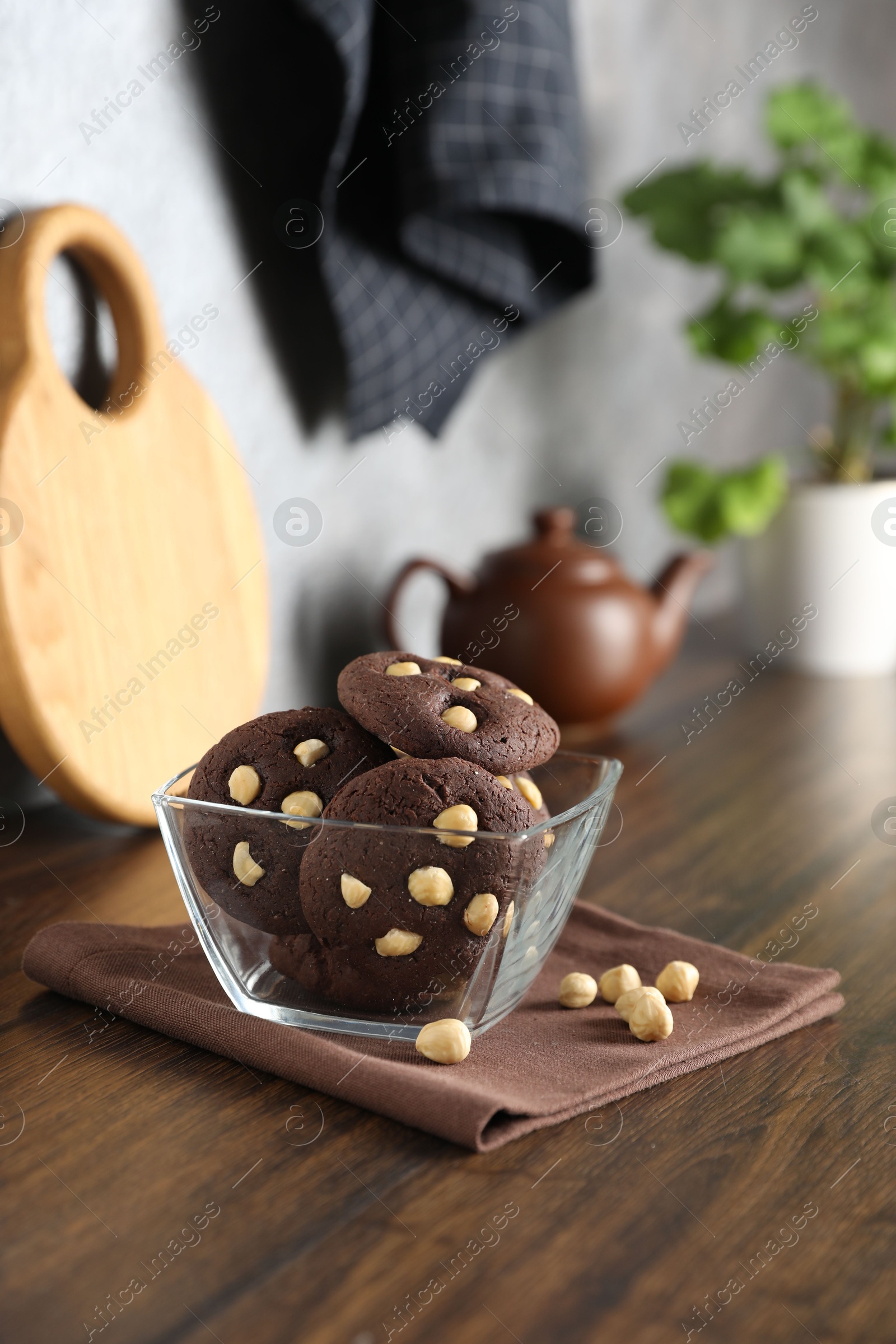 Photo of Tasty chocolate cookies with hazelnuts in bowl on wooden table