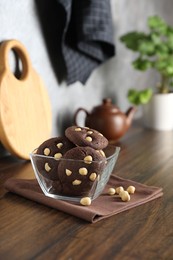 Photo of Tasty chocolate cookies with hazelnuts in bowl on wooden table