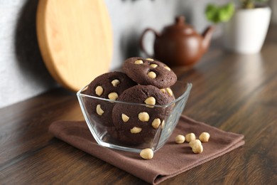 Photo of Tasty chocolate cookies with hazelnuts in bowl on wooden table, closeup