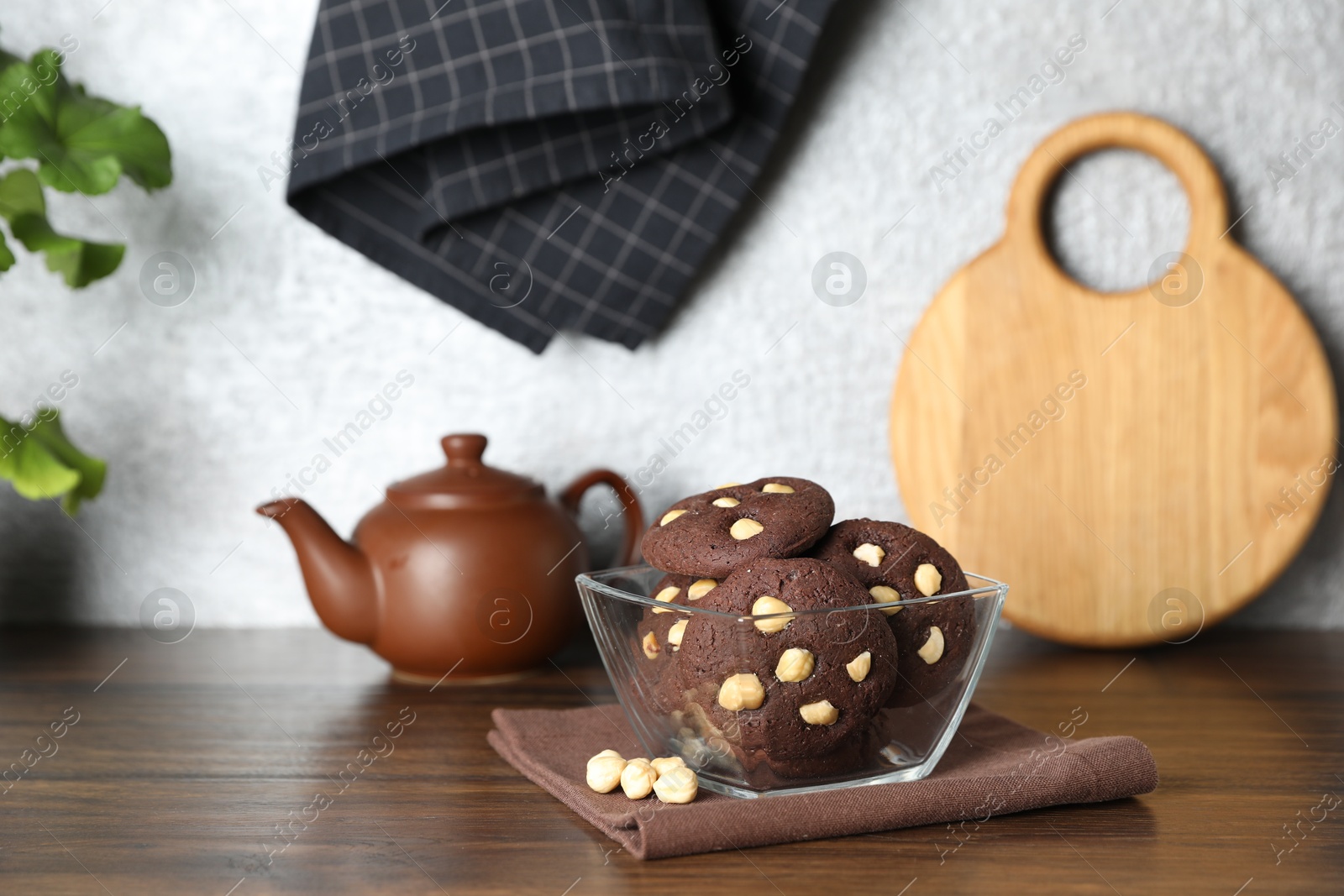 Photo of Tasty chocolate cookies with hazelnuts in bowl on wooden table