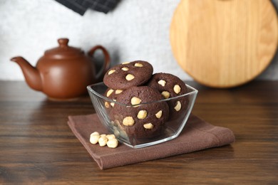 Photo of Tasty chocolate cookies with hazelnuts in bowl on wooden table