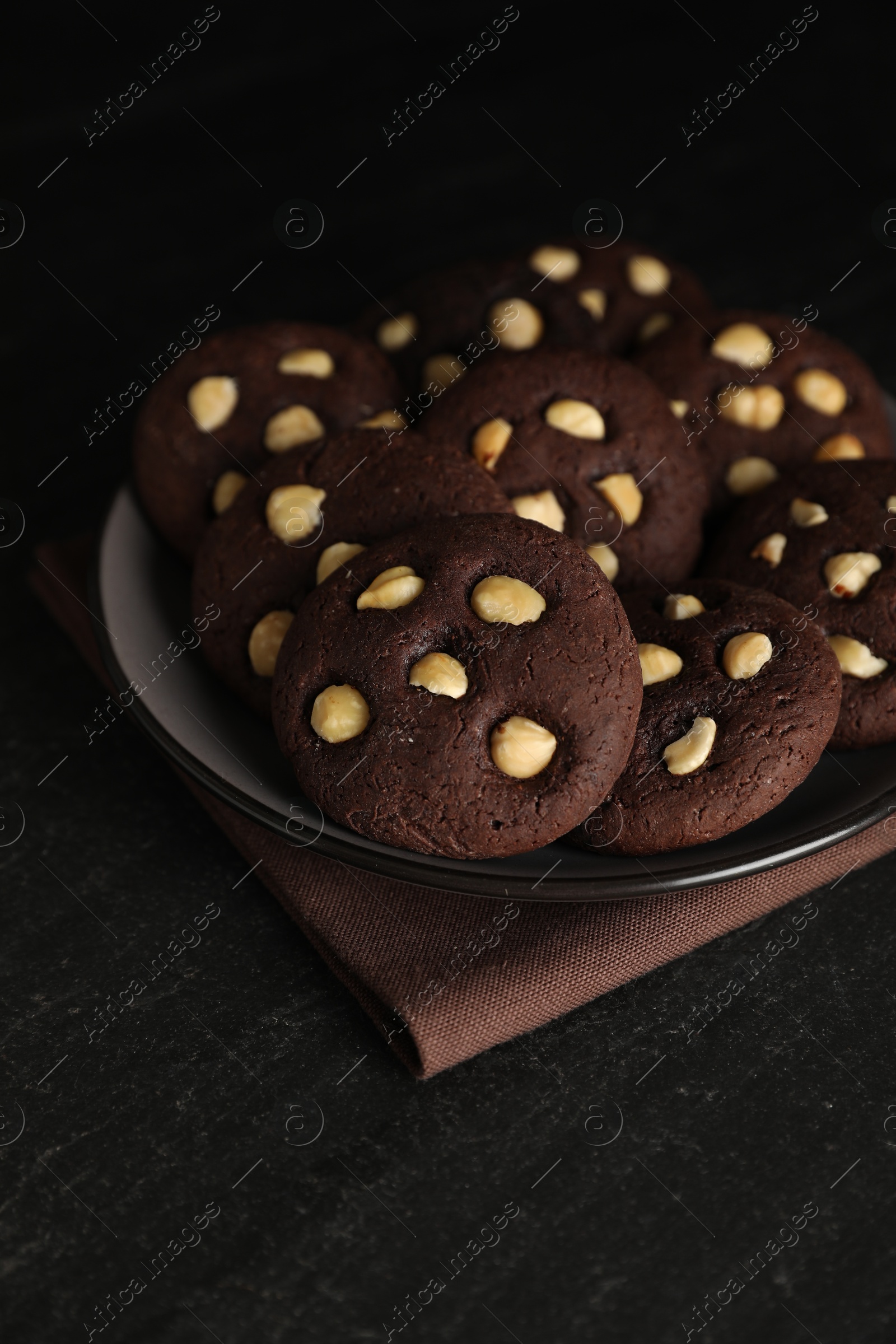 Photo of Tasty chocolate cookies with hazelnuts on black table, closeup