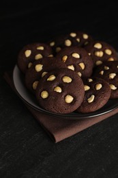 Photo of Tasty chocolate cookies with hazelnuts on black table, closeup