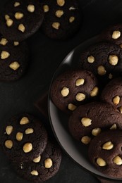 Photo of Tasty chocolate cookies with hazelnuts on black table, flat lay