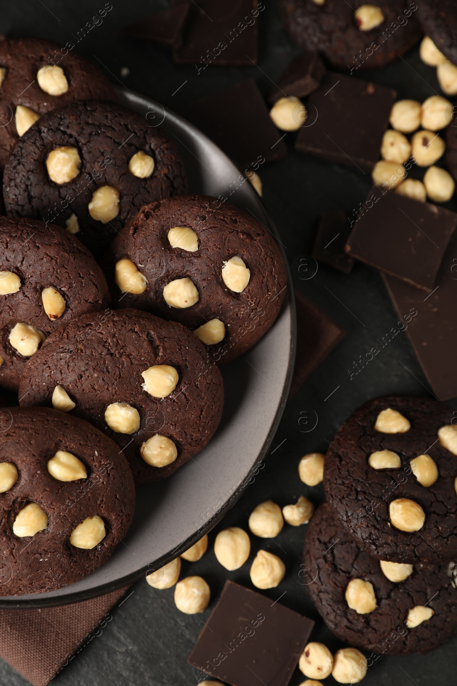 Photo of Tasty chocolate cookies with hazelnuts on black table, flat lay