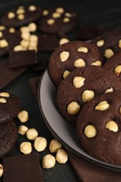 Photo of Tasty chocolate cookies with hazelnuts on black table, closeup