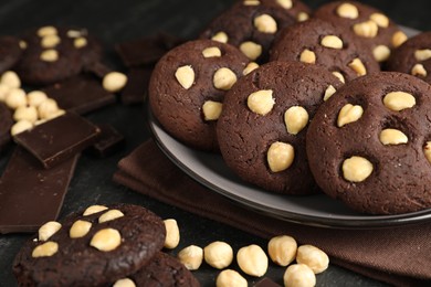 Photo of Tasty chocolate cookies with hazelnuts on black table, closeup