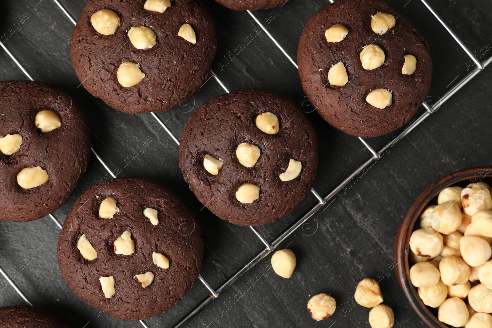 Photo of Tasty chocolate cookies with hazelnuts on black table, flat lay