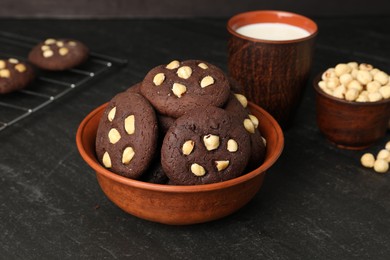 Photo of Tasty chocolate cookies with hazelnuts and milk on black table, closeup