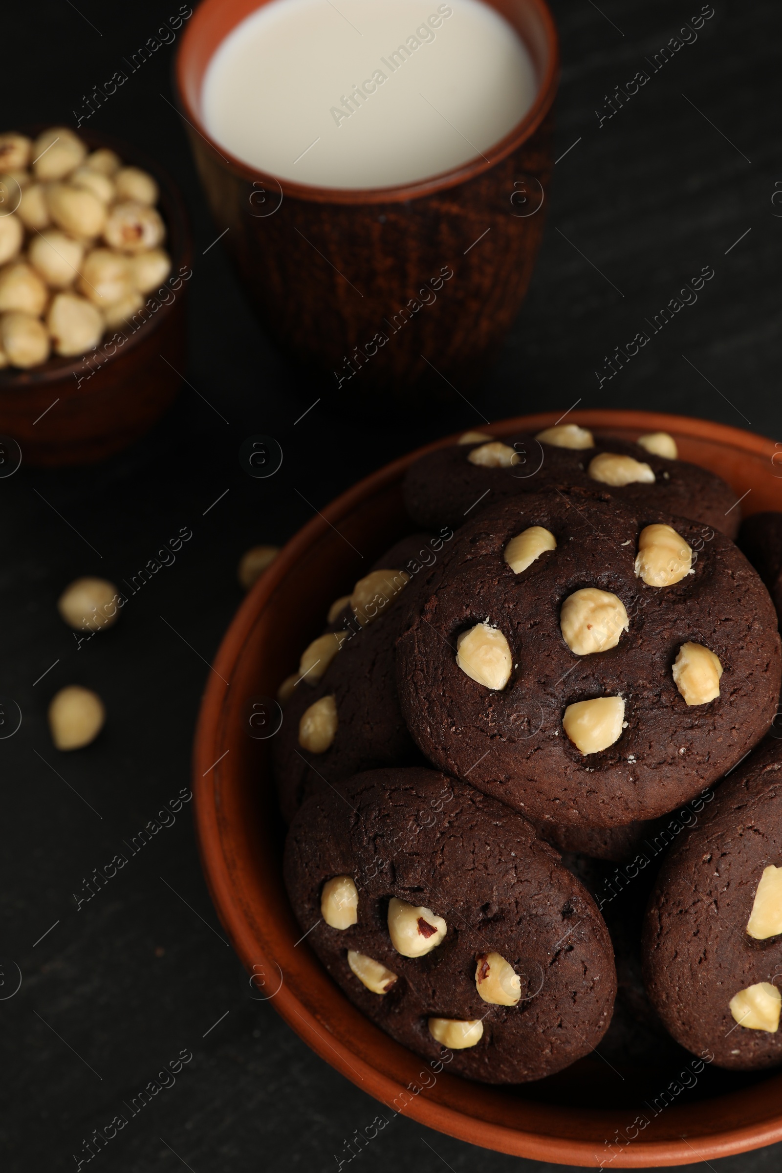 Photo of Tasty chocolate cookies with hazelnuts and milk on black table, closeup