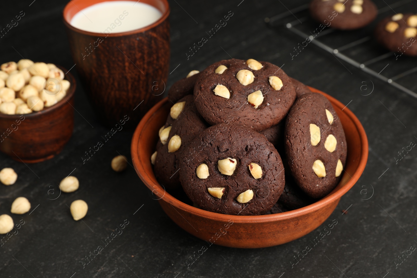 Photo of Tasty chocolate cookies with hazelnuts and milk on black table, closeup