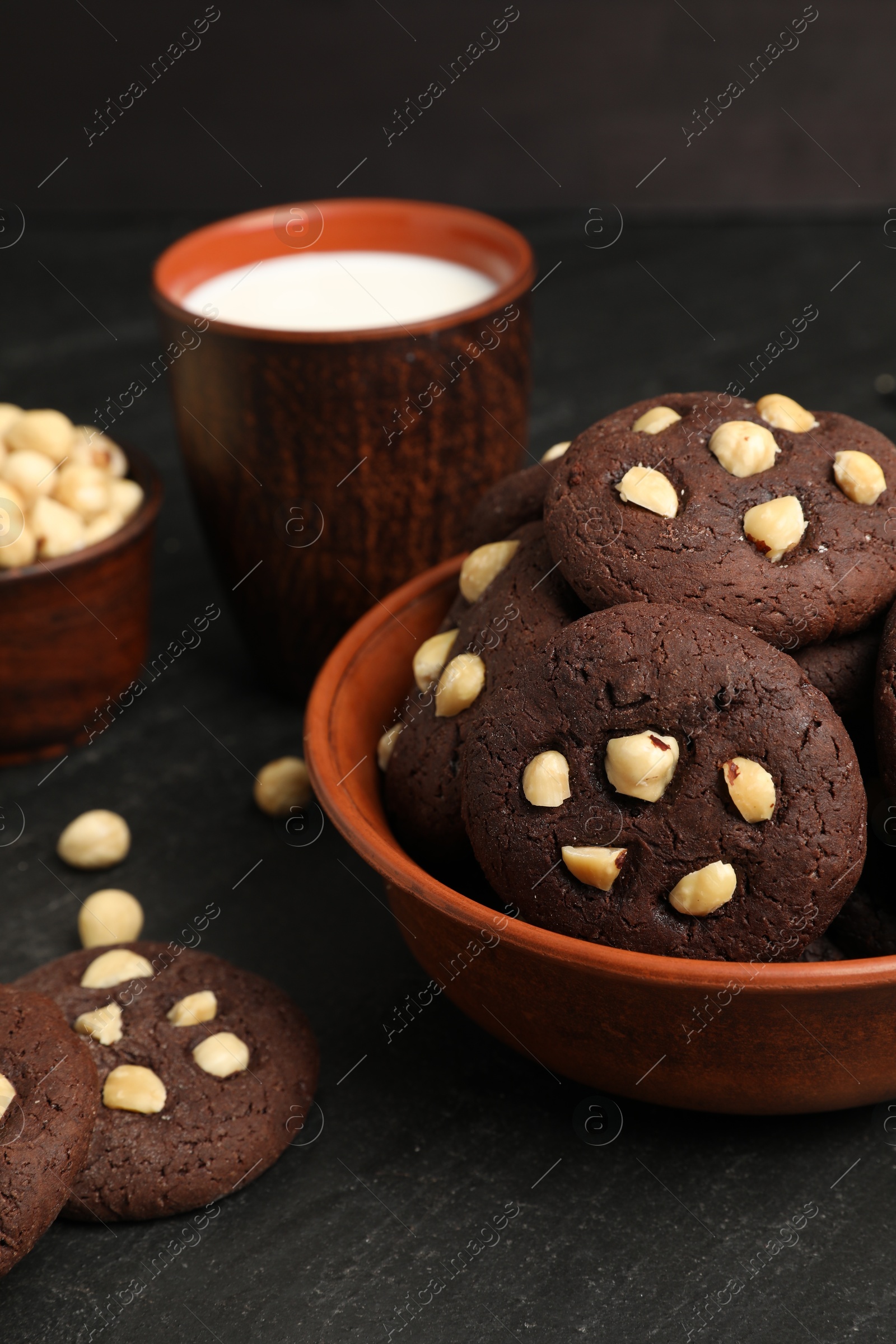 Photo of Tasty chocolate cookies with hazelnuts and milk on black table, closeup