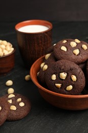 Photo of Tasty chocolate cookies with hazelnuts and milk on black table, closeup