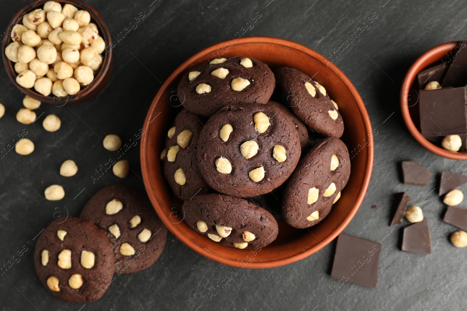 Photo of Tasty chocolate cookies with hazelnuts on black table, flat lay