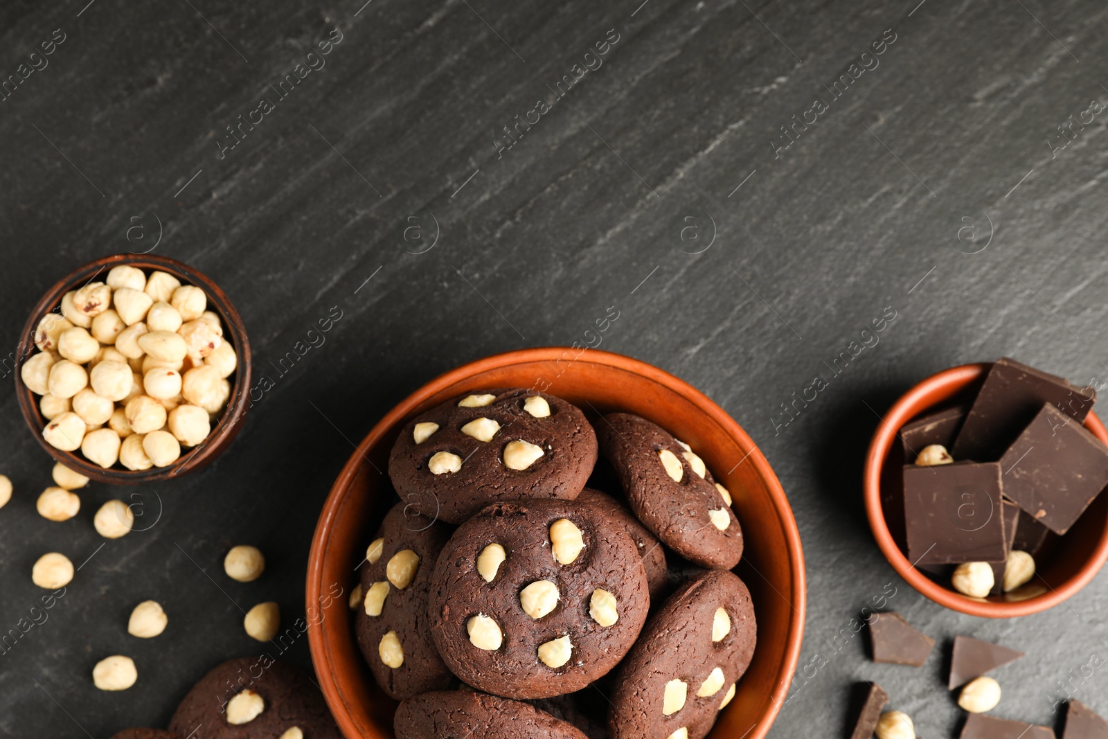 Photo of Tasty chocolate cookies with hazelnuts on black table, flat lay. Space for text