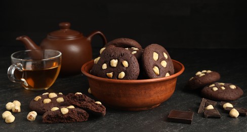 Photo of Tasty chocolate cookies with hazelnuts and tea on black table