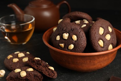 Photo of Tasty chocolate cookies with hazelnuts and tea on black table, closeup