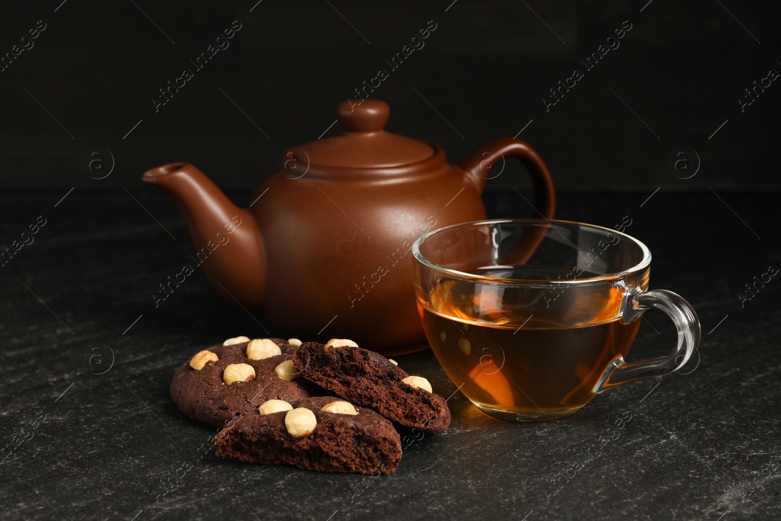 Photo of Tasty chocolate cookies with hazelnuts and tea on black table