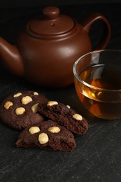 Photo of Tasty chocolate cookies with hazelnuts and tea on black table, closeup