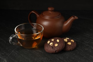 Photo of Tasty chocolate cookies with hazelnuts and tea on black table