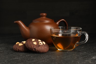 Photo of Tasty chocolate cookies with hazelnuts and tea on black table