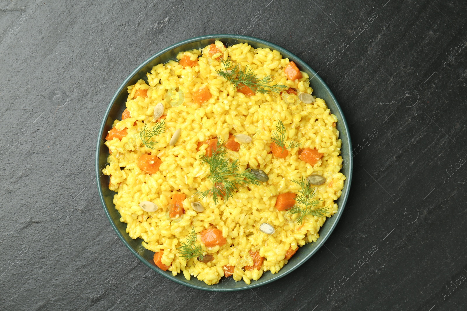 Photo of Delicious pumpkin risotto in bowl on black table, top view