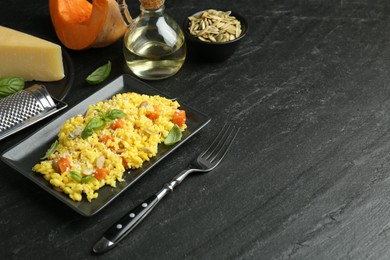 Photo of Delicious pumpkin risotto served on black table. Space for text