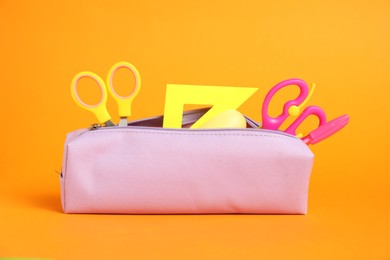 Photo of Different stationery in pencil case on orange background