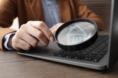 Image of Search for housing. Real estate agent holding magnifying glass with building icon over laptop, closeup