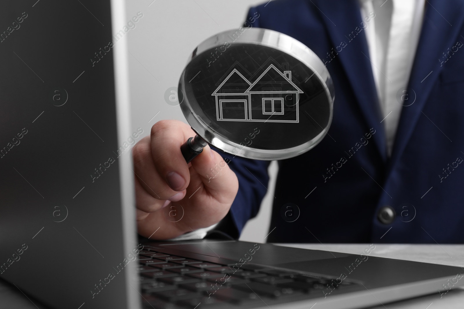 Image of Search for housing. Real estate agent holding magnifying glass with building icon over laptop, closeup