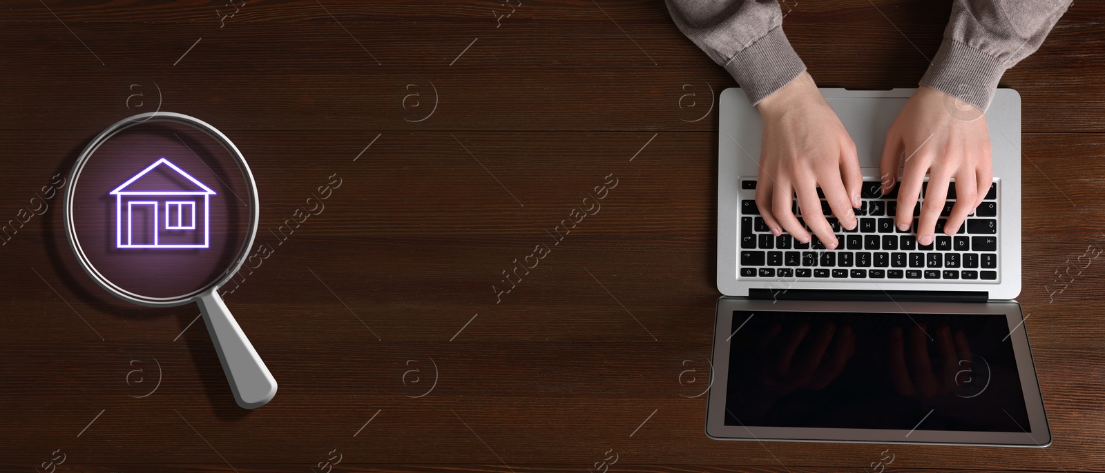 Image of Search for housing. Real estate agent using laptop at wooden table, top view. Magnifying glass with building icon