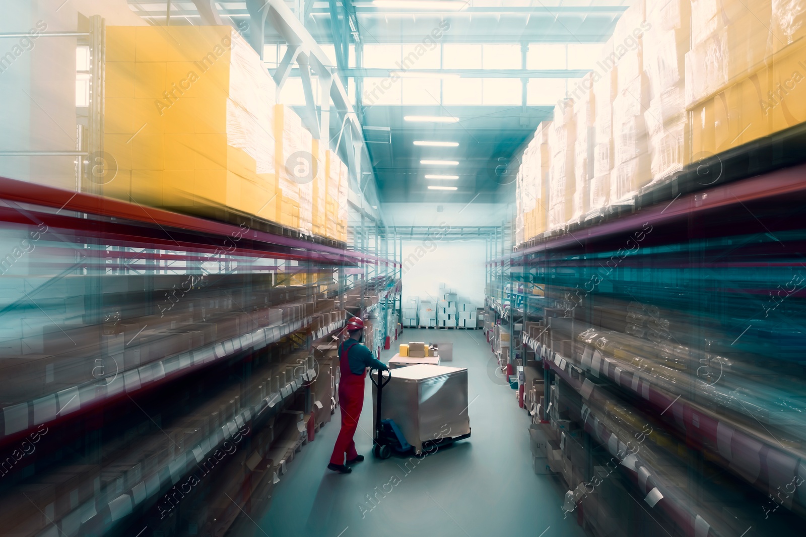 Image of Man in hardhat working with pallet truck at warehouse. Logistics center