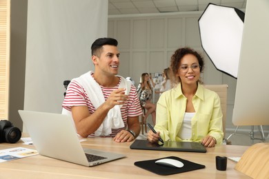 Professional retoucher with colleague working at desk in photo studio