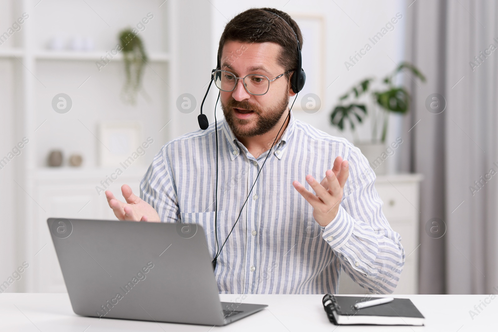 Photo of Interpreter in headset having video chat via laptop at white table indoors