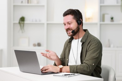 Interpreter in headset having video chat via laptop at white table indoors