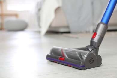 Photo of Cleaning floor with cordless vacuum cleaner indoors, closeup. Space for text