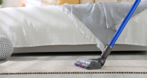 Photo of Cleaning carpet with cordless vacuum cleaner indoors, closeup. Space for text