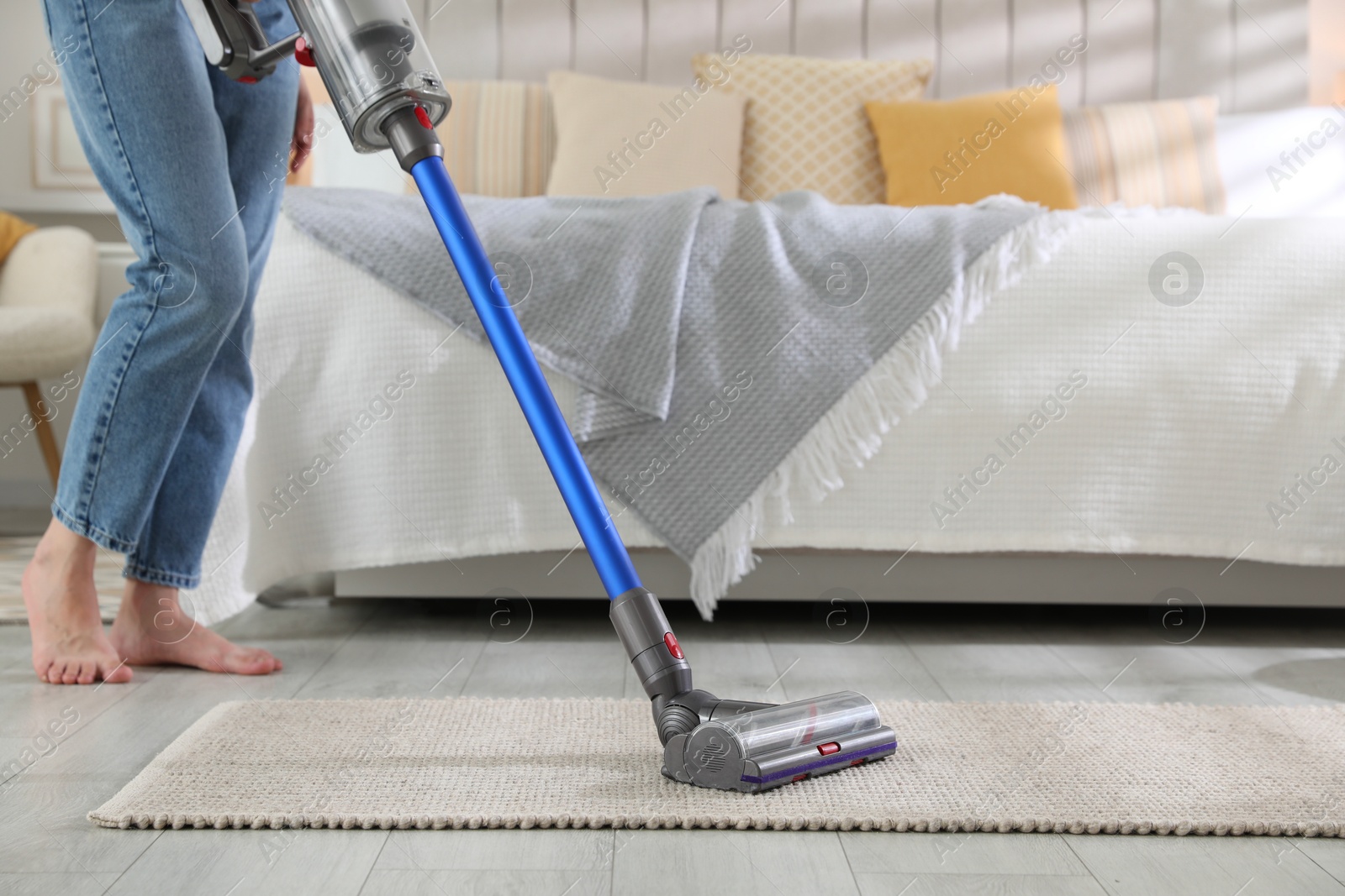 Photo of Woman cleaning rug with cordless vacuum cleaner indoors, closeup. Space for text