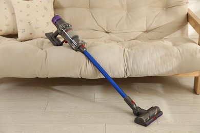 Photo of One cordless vacuum cleaner leaning on sofa indoors