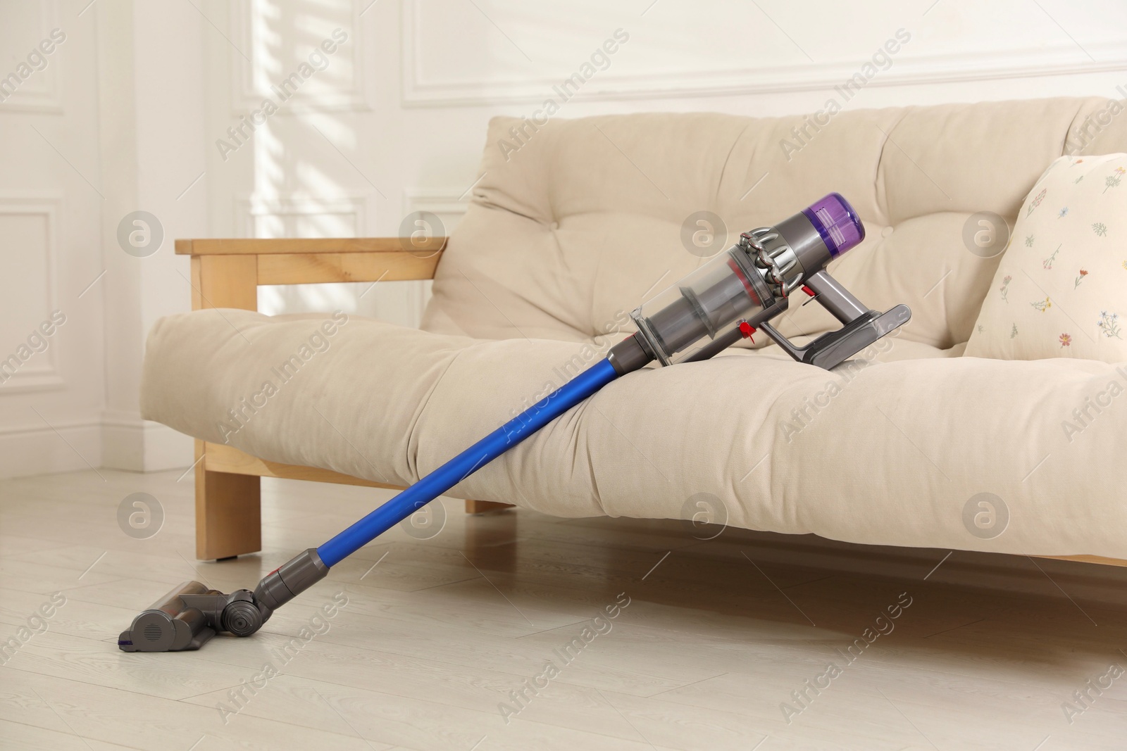 Photo of One cordless vacuum cleaner leaning on sofa indoors