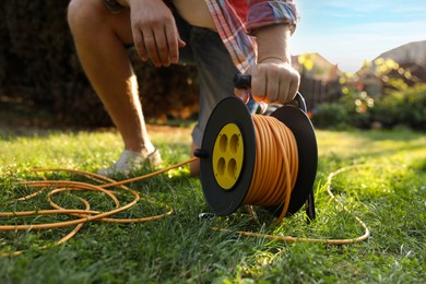 Photo of Man with extension cord reel on green grass outdoors, closeup