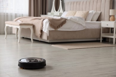 Robotic vacuum cleaner on wooden floor in bedroom